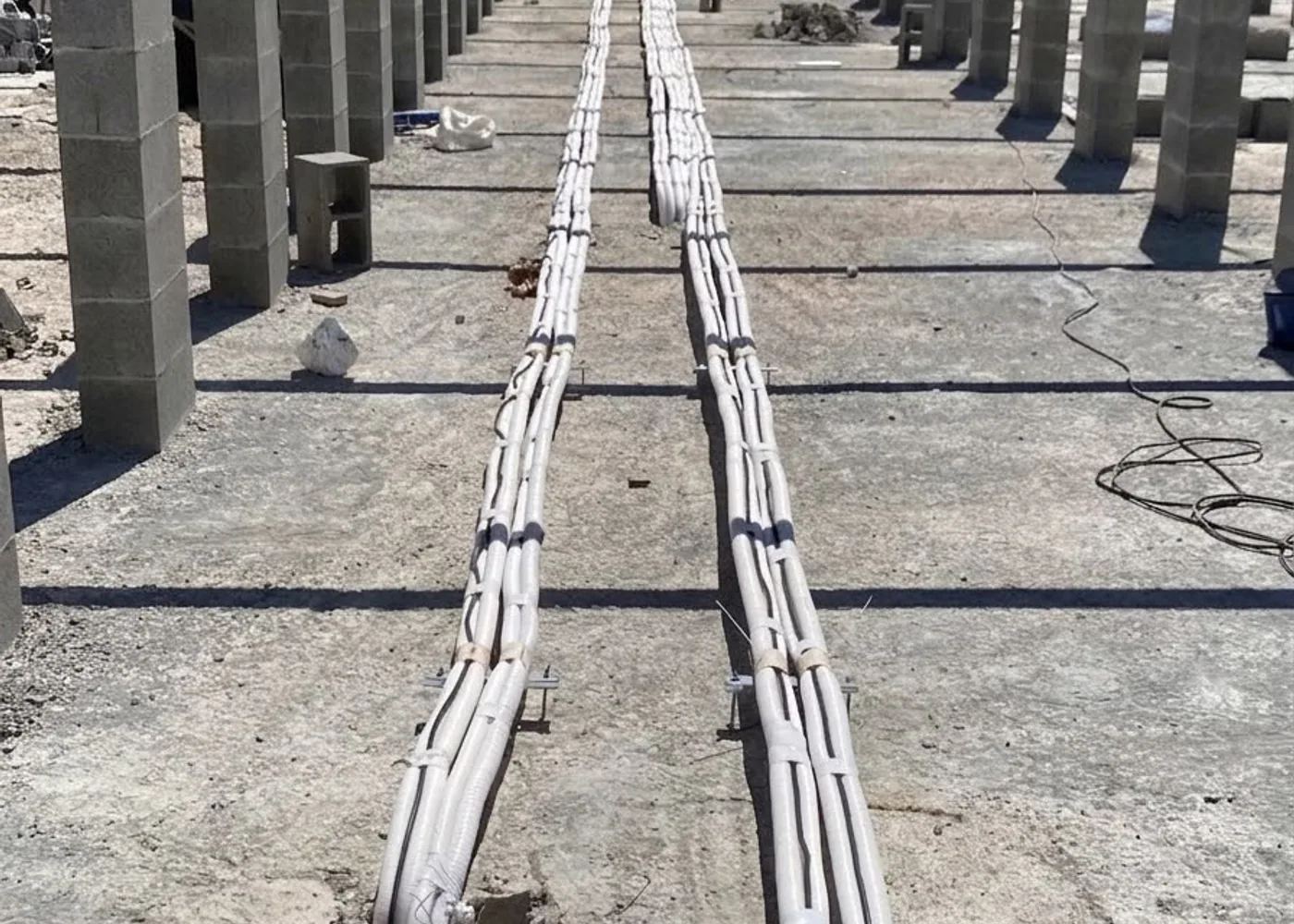 Linhas frigoríficas isoladas correndo pela laje de uma instituição de ensino, entre pilares de concreto.