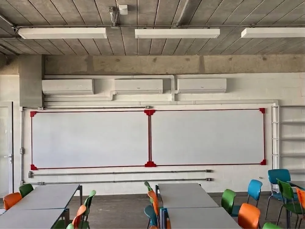 Sala de aula com unidade split instalada em altura e cadeiras coloridas.